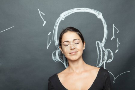 Photo for Dark-haired girl pretends to listen to music thanks to headphones designed on the dark background - Royalty Free Image