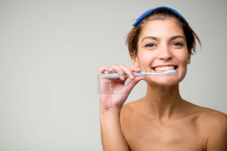 Téléchargez les photos : Belle fille aux cheveux courts se brosse les dents avec une brosse à dents, isolée sur fond clair - en image libre de droit
