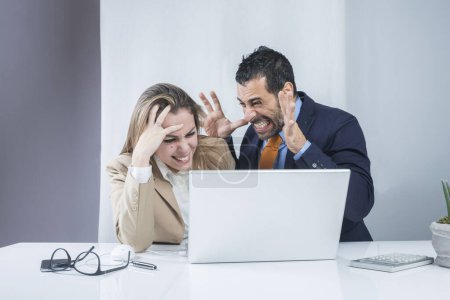 Téléchargez les photos : Paire de collègues d'affaires sont heureux des résultats obtenus se disputant furieusement assis dans le bureau devant le bureau avec un ordinateur portable - en image libre de droit