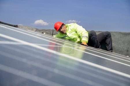 Foto de Trabajador con casco protector rojo, mono especialista y gafas técnicas trabaja en un sistema fotovoltaico instalado en el techo de un edificio - Imagen libre de derechos