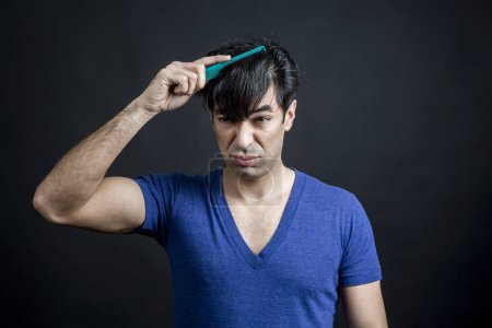 Téléchargez les photos : Jeune homme beau avec une brosse à cheveux sur un fond gris - en image libre de droit