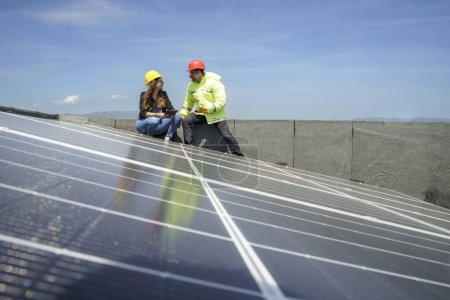 Téléchargez les photos : Un ingénieur avec un travailleur vérifie l'installation de panneaux photovoltaïques sur le toit d'un bâtiment - en image libre de droit
