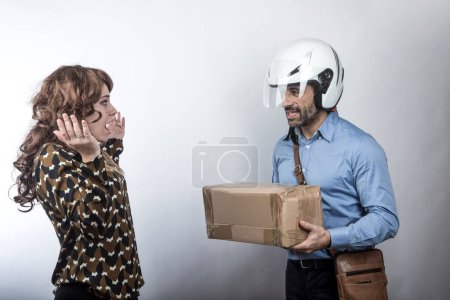 Téléchargez les photos : Messager avec casque fait la livraison d'un colis à une dame étonnée, isolé sur fond blanc - en image libre de droit