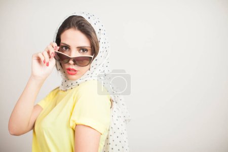 Foto de Chica rubia con pañuelo en la cabeza y camisa amarilla vestida al estilo de los años 50 aislada sobre fondo gris - Imagen libre de derechos