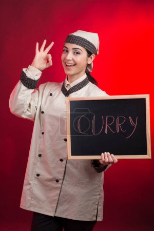Foto de Cocinero hace la señal ok con la celebración de una pizarra con "Curry" escrito en él, aislado sobre fondo rojo - Imagen libre de derechos