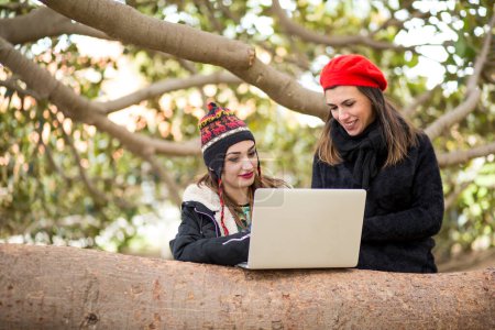 Téléchargez les photos : Portrait de jeunes étudiants utilisant un ordinateur portable sur le tronc d'arbre dans le parc - en image libre de droit