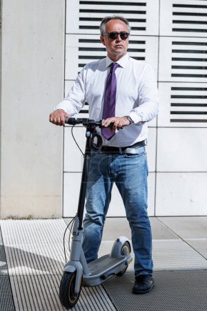 Téléchargez les photos : Homme mature avec scooter électrique sur la rue de la ville - en image libre de droit