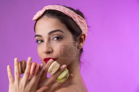 Photo for Beautiful girl with white with black hair and light shirt, plays and has fun with colorful macarons, isolated on purple background - Royalty Free Image
