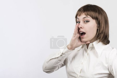 Foto de Chica de pelo rubio con el pelo bob y camisa blanca gritando algo mientras que trae mano a boca, aislado sobre fondo blanco - Imagen libre de derechos