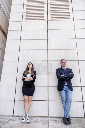 Foto de Un hombre y una mujer elegantemente vestidos se apoyan contra la pared de una estructura moderna - Imagen libre de derechos