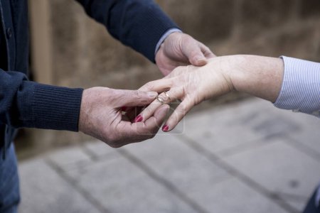 Foto de Detalle de las manos de un anciano que se pone un anillo en el dedo a su anciana novia en un contexto urbano - Imagen libre de derechos