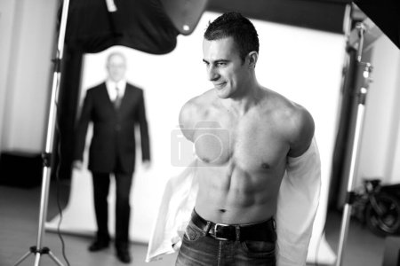 Téléchargez les photos : Portrait noir et blanc d'un homme élégant déshabillé enlevant sa chemise à l'intérieur d'un studio photo - en image libre de droit