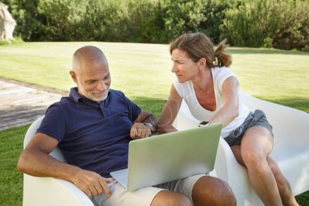 Téléchargez les photos : Couple regarde quelque chose d'intéressant dans l'ordinateur portable assis relaxant dans le jardin de la maison - en image libre de droit
