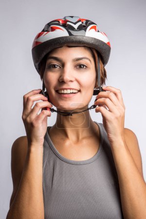 Photo for Smiling woman cyclist fastens the technical helmet, isolated on light background - Royalty Free Image