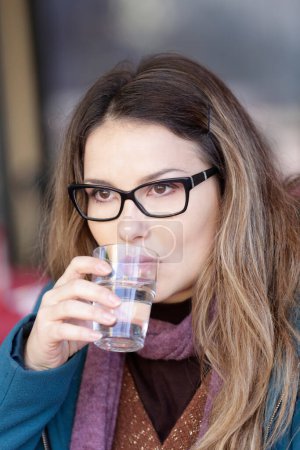 Téléchargez les photos : Portrait de belle fille belle avec des cheveux lâches boire un verre d'eau assis dans un bar - en image libre de droit