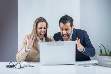 Photo for Pair of business colleagues are happy with the results achieved arguing furiously sitting in the office in front of the desk with a laptop - Royalty Free Image