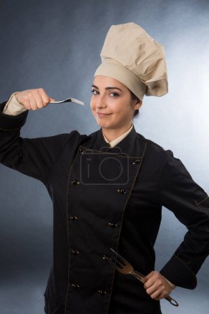 Foto de Mujer chef prueba un plato de una cuchara, aislado sobre fondo gris - Imagen libre de derechos