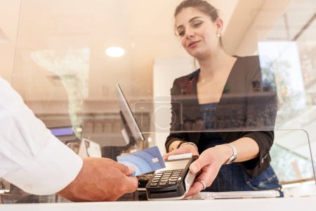 Foto de Vendedora en una tienda de pago recibe el pago de un cliente que paga con tarjeta de crédito. - Imagen libre de derechos