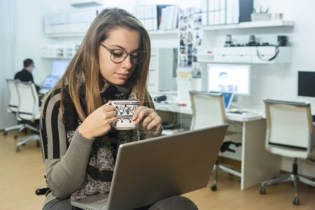 Foto de Chica rubia con gafas, y camisa a rayas trabaja con expresión seria sentado frente a la computadora en su oficina lugar de trabajo - Imagen libre de derechos