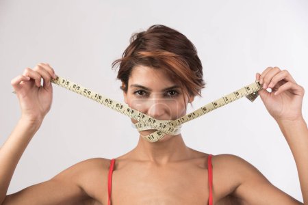 Photo for Girl in red bikini turns around a meter dressmaker's face to indicate the only way to do the diet, or not to eat, isolated on a light background - Royalty Free Image