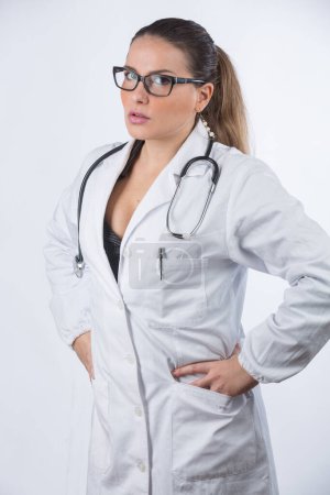 Téléchargez les photos : Portrait de belle femme blonde médecin avec des lunettes et les cheveux rassemblés regardant avec une expression sérieuse, isolé sur fond blanc - en image libre de droit