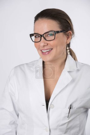 Téléchargez les photos : Portrait de belle femme blonde médecin avec des lunettes et les cheveux rassemblés regardant avec un beau sourire, isolé sur fond blanc - en image libre de droit