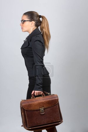 Téléchargez les photos : Femme d'affaires blanche avec les cheveux et les lunettes réunis, vêtue d'un costume noir et chemise à motifs, marche avec une garniture en cuir, isolé sur fond blanc - en image libre de droit