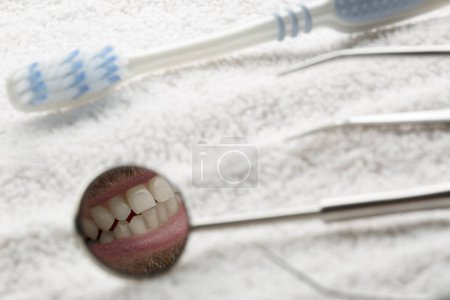 Téléchargez les photos : Détails d'une brosse à dents et d'un miroir de dentiste reflétant un sourire, isolés sur une serviette - en image libre de droit