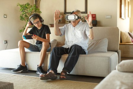 Foto de Abuelo y nieto juegan juegos electrónicos sentados en el sofá en la sala de estar - Imagen libre de derechos