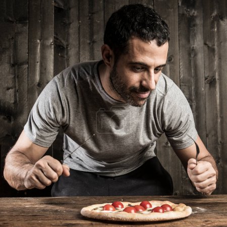 Photo for Dark-haired man with a beard is about to eat a pizza with cherry tomatoes, isolated on wood background - Royalty Free Image
