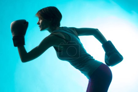 Photo for Beautiful girl with bob hair and boxing gloves holds gurdia high, isolated on blue background - Royalty Free Image