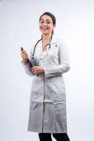 Foto de La doctora blanca de pelo negro con una bata blanca, anteojos y un estetoscopio en el cuello está aislada sobre un fondo blanco - Imagen libre de derechos