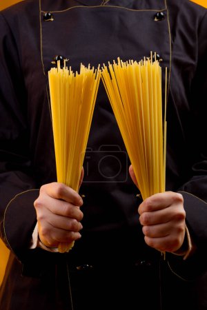 Foto de Chef sostiene espaguetis crudos en la mano que ella sostiene, aislado sobre fondo naranja - Imagen libre de derechos