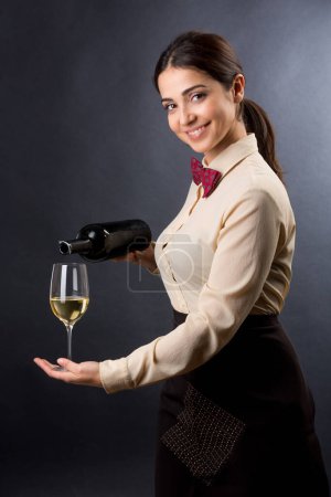 Téléchargez les photos : Belle et élégante serveuse avec chemise et nœud papillon rouge est prête à offrir un verre de vin, isolé sur un fond noir - en image libre de droit