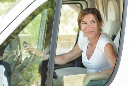 Téléchargez les photos : Dame blanche en chemise blanche regarde par la fenêtre assise derrière le volant de son camping-car - en image libre de droit
