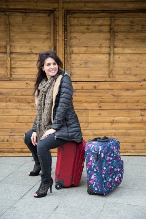 Téléchargez les photos : Touriste en vêtements d'hiver est assis sur le dessus des valises en face d'un kiosque en bois dans une place - en image libre de droit