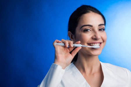 Photo for Smiling woman dentist on light blue background and toothbrush. - Royalty Free Image