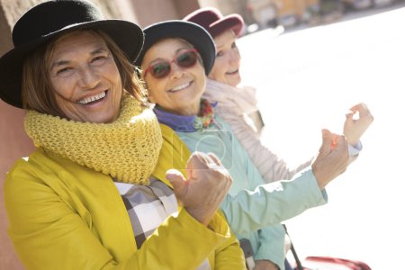 Téléchargez les photos : Touristes âgés avec des chapeaux et des vêtements colorés s'amuser autour de la ville avec leurs valises - en image libre de droit