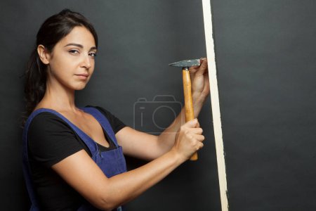 Photo for White girl with black hair beats a nail with a hammer, isolated on a black background - Royalty Free Image