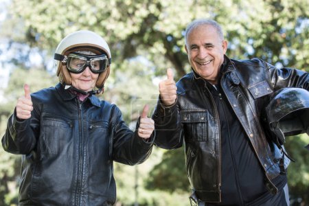 Foto de Retrato de pareja mayor con casco protector mostrando los pulgares hacia arriba mientras está sentado en moto - Imagen libre de derechos