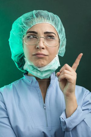 Foto de Médico en bata de laboratorio azul y máscara facial blanca trae su mano a la cabeza en la desesperación, aislado sobre fondo verde - Imagen libre de derechos