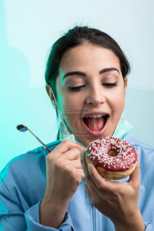 Photo for Dentist with lab coat eats a donut on green background - Royalty Free Image