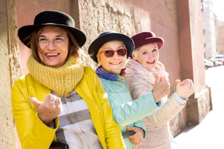 Téléchargez les photos : Touristes âgés avec des chapeaux et des vêtements colorés s'amuser autour de la ville avec leurs valises - en image libre de droit