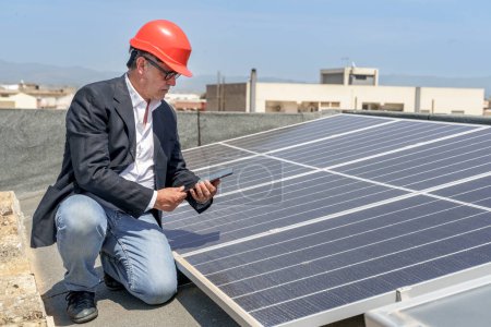 Foto de Ingeniero comprueba las condiciones de un sistema fotovoltaico en el techo de una casa con una tableta en la mano - Imagen libre de derechos
