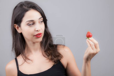Téléchargez les photos : Jeune et belle fille brune mange une fraise - en image libre de droit