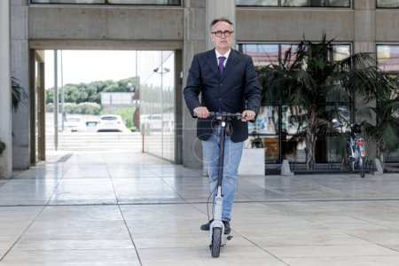 Foto de Elegante gerente vestido se mueve rápidamente con su scooter eléctrico en un entorno urbano moderno - Imagen libre de derechos