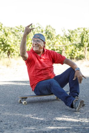 Photo for Senior in red jersey enjoys skateboarding on a country road - Royalty Free Image