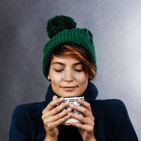 Téléchargez les photos : Belle fille avec chapeau vert et pull bleu prend le thé en détente, isolé sur fond gris - en image libre de droit