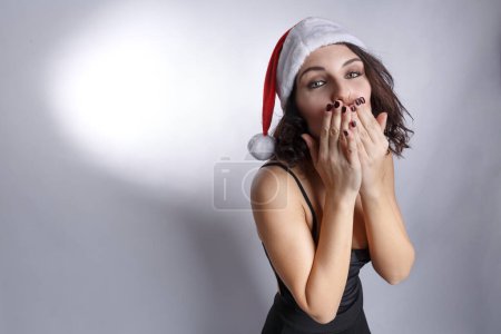 Photo for Beautiful brunette girl in a black dress and santa hat is dancing and having fun, isolated on white background. - Royalty Free Image