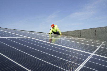 Photo for Worker with red protective helmet, specialist overalls and technical goggles works on a photovoltaic system installed on the roof of a building - Royalty Free Image